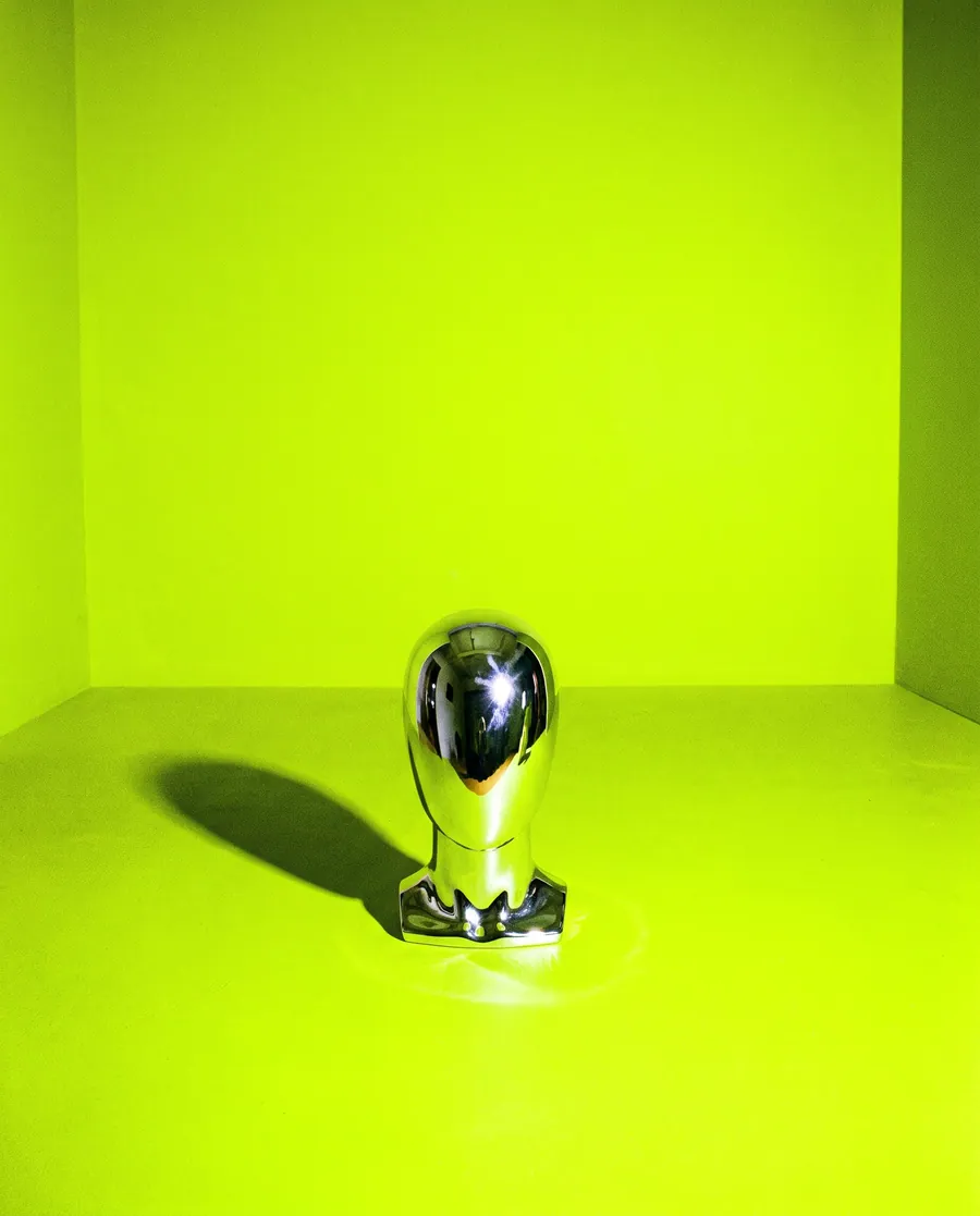 A chrome object standing on an acid green floor